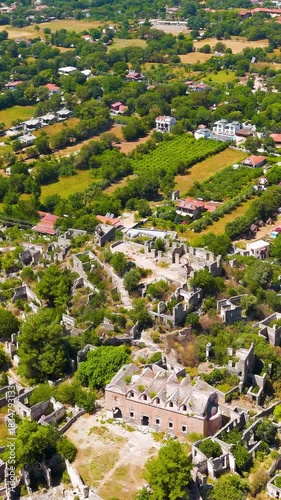 Vertical video. Kayakoy, Turkey. Aerial drone view of the Upper Church (Panagia Pyrgiotissa) among abandoned ghost town ruins on mountain slope under clear sky.. Aerial View, Point of interest. Rich 