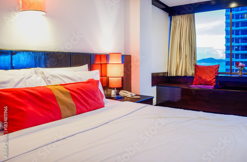 Luxurious Hotel Bedroom Interior with City View and Warm Lighting. Elegant and modern upscale hotel or apartment bedroom with a comfortable bed and a large window overlooking a dramatic city skyline.