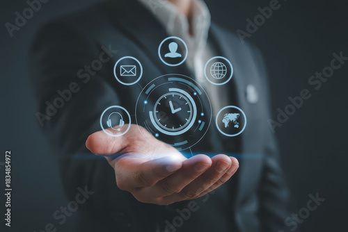 Professional suit holds holographic display featuring various digital icons, symbolizing communication, time management, and global connectivity. This futuristic concept represents modern digital