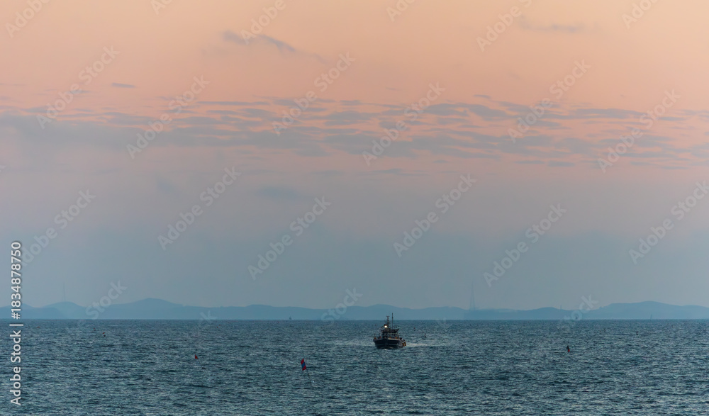 Fototapeta premium A Boat Passing Over the Sea Under an Orange Sunset Sky