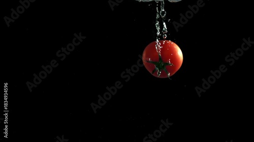 Fresh tomatoes falling under water on a black background. Filmed on a high-speed camera at 1000 fps. High quality FullHD footage