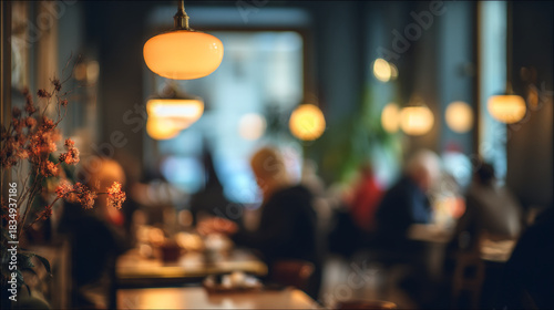 Blurred interior of a restaurant with people dining under warm lighting and floral decorations visible