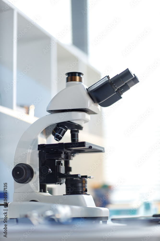 Fototapeta premium Laboratory microscope standing on table in scientific research setting, optical device featuring multiple objective lenses and adjustment knobs, used for biological or medical analysis