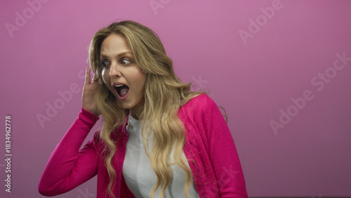 Foto Young blonde woman in pink cardigan listening with curiosity against an isolated pink background wall conveying surprise and attention