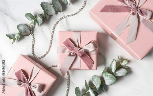 Elegant pink gift boxes with velvet ribbons and eucalyptus leaves on a white marble background.