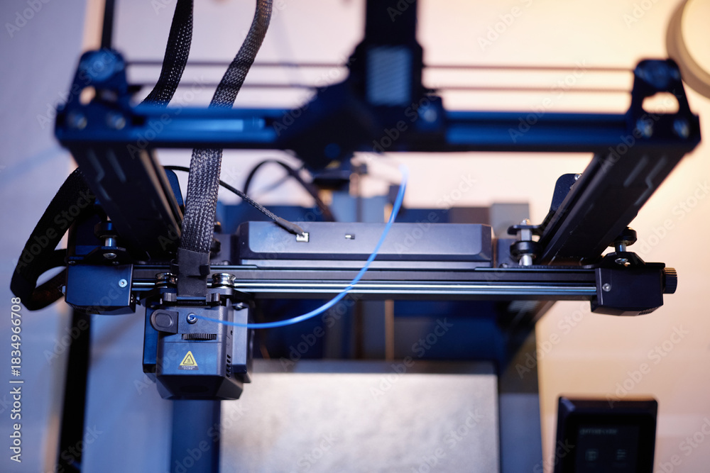 Fototapeta premium Closeup showing 3D printer operating with extruder head moving along rails, filament feeding through mechanism, advanced manufacturing technology in modern workspace