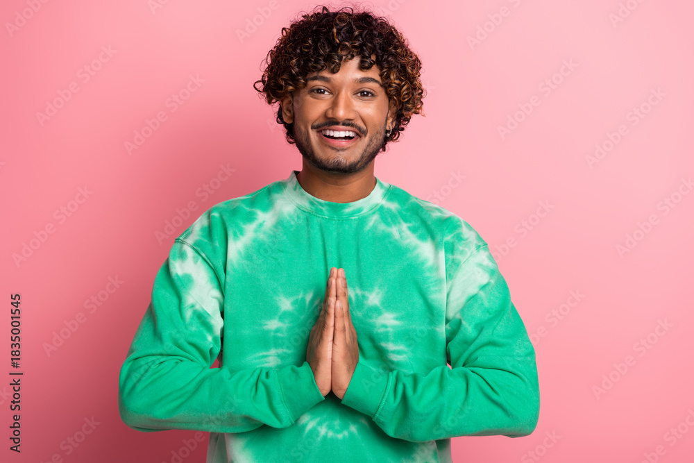 Fototapeta premium Young male model in green tie dye sweater smiling hands pressed together in greeting against pink background fashion lifestyle advertising casual campaigns