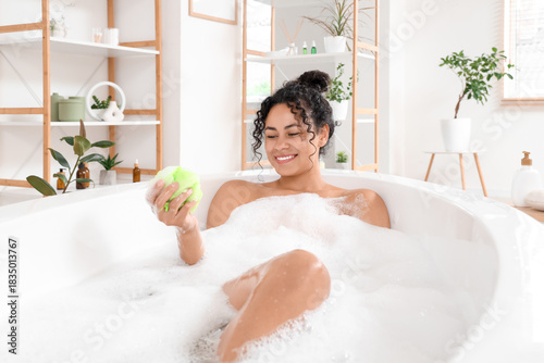 Fotografie Beautiful young happy African-American woman taking bath with sponge and soap fo