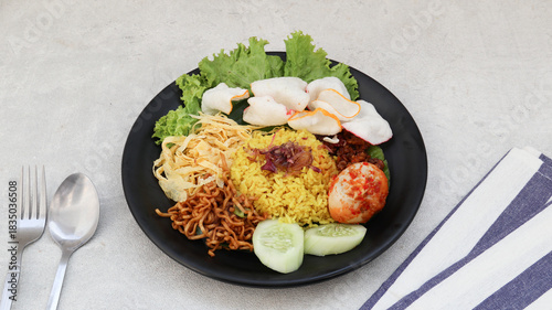 Indonesian traditional food, nasi kuning yellow turmeric rice served with vegetables, spicy eggs, noodles and tempeh