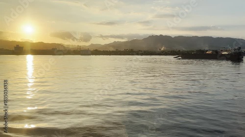 Serene Sunset Splendor: Tranquil Waters Reflecting Golden Light Against Majestic Mountains and a Distant Shoreline