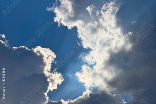Sunbeams break dramatically through dense clouds in the blue sky.