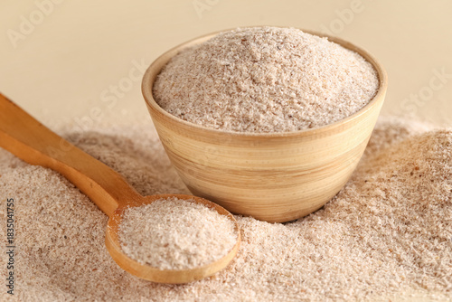 Bowl and spoon with psyllium husk powder on beige background, closeup