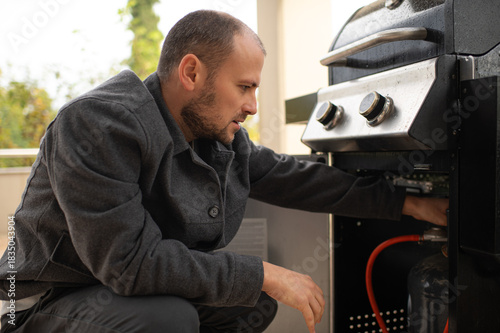 Εκτύπωση καμβά Man inspecting a barbecue grill on a sunny terrace, preparing food for outdoor cooking, home leisure, summer lifestyle