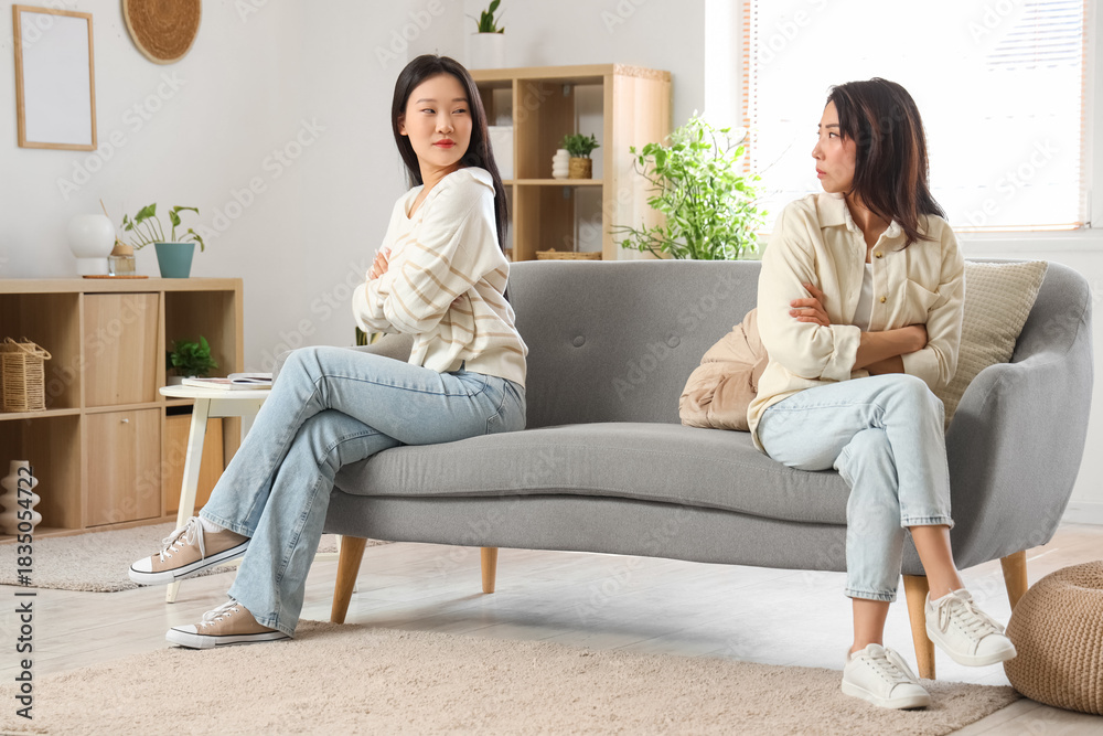 Obraz premium Beautiful young sad Asian sisters sitting on sofa at home