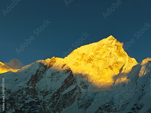 Majestic snow-capped mountain peak illuminated by golden sunlight against a clear blue sky, showcasing the beauty of nature and the grandeur of the landscape
