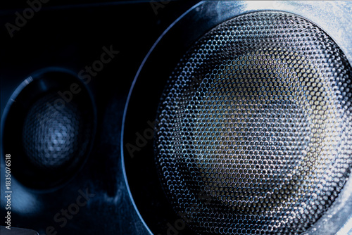 Close-up of two audio speakers with perforated metallic mesh in low light