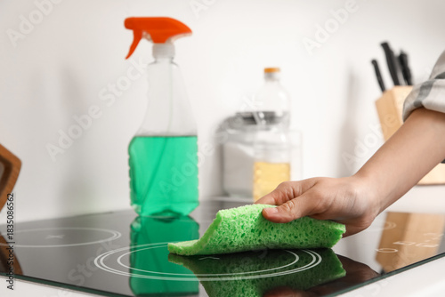 Fotografía Woman cleaning glass ceramic induction cooktop with sponge and spray cleaner in