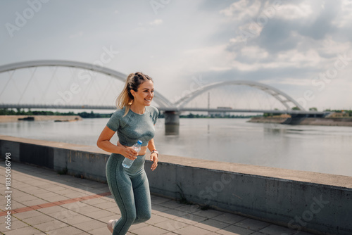 Young sporty woman running near river with bridge in background