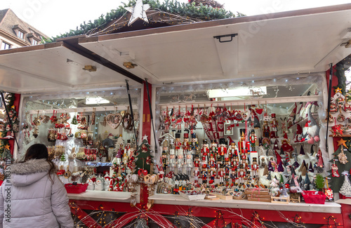 Nutcrackers, snowmen, dwarfs, Christmas balls and other festive ornaments for sale at traditional Christmas market in Strasbourg, France. Unrecognizable woman choosing to buy a gift.