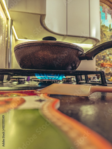 Cooking pan with lid heating on a gas burner with a bright blue flame in a kitchen setting.