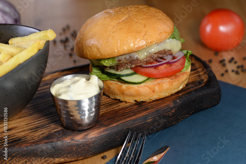 large cheeseburger with tomato on a wooden board with sauce and french fries macro