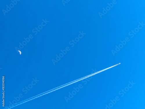 Holiday jet in flight with twin contrails passing the moon on a deep blue sky