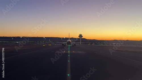 An cockpit view through the pilot’s eyes while taxiing behind a twin-engine jet through the taxiways of Madrid airport at sunrise.