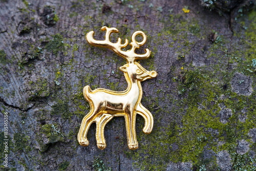 A statuette of a metal deer on the bark of a tree.