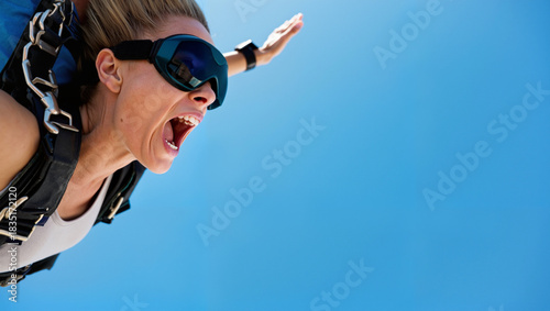 Young woman skydiving, feeling excitement, free falling against blue sky with copy space