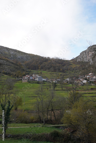 Serene La Hermida Valley Nestles Among Limestone Peaks - Mountainous landscape with farm, scattered houses, and trees features lush greens and grey mountains in a tranquil rural setting.