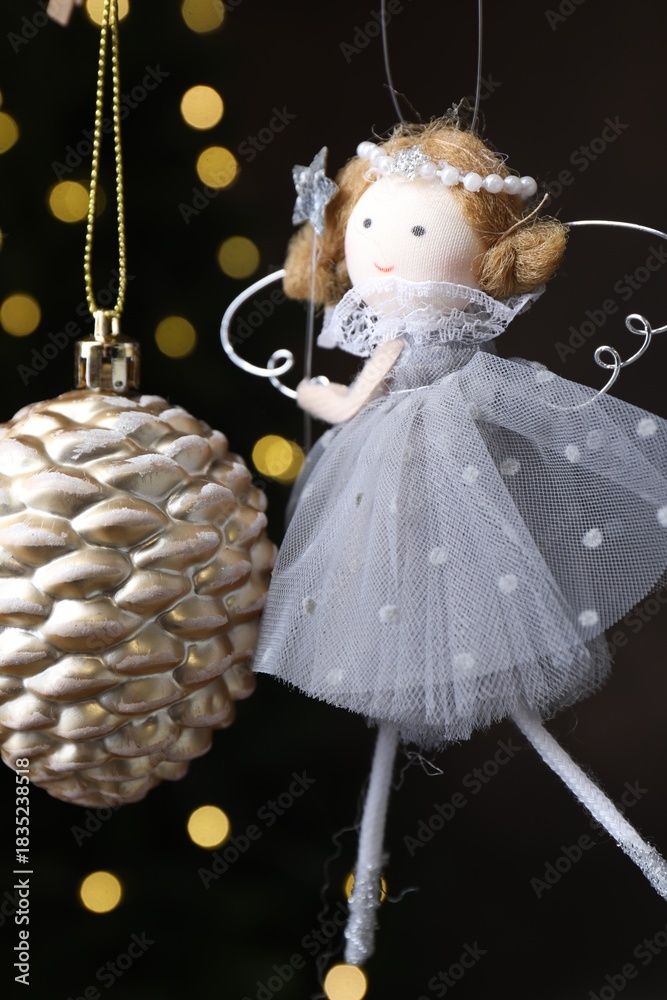 Obraz premium Beautiful Christmas bauble and fairy doll hanging against black background with blurred lights, closeup