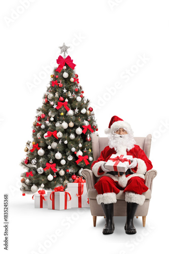 Santa claus sitting in armchair with a present in front of a Christmas tree
