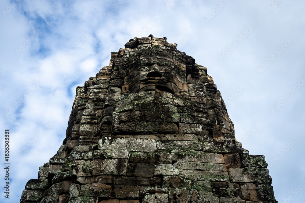 Fototapeta premium Ancient stone face of Bayon temple in Angkor, Cambodia, against a cloudy sky