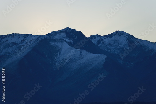 Φωτογραφία Lake Pukaki, NZ - May 24, 2025: A dramatic twilight close-up of dark, snow-dusted mountain peaks silhouetted against a pale sky