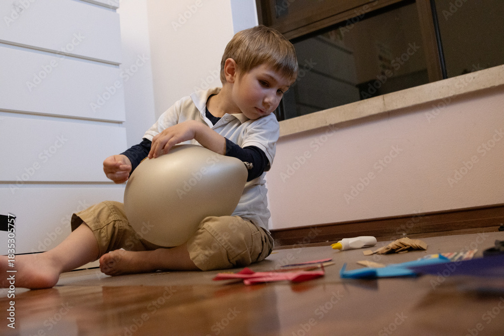 Naklejka premium Young boy playing on floor with balloon and craft supplies