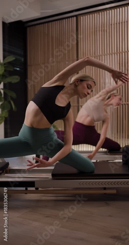 Engaging Pilates class shows two women performing a series of exercises on reformers in a spacious studio with natural light. Focus on flexibility and strength