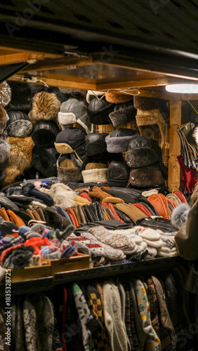 Vibrant assortment of fur hats, leather caps, knit scarves, knitted woolen mittens and gloves displayed in a bustling christmas market stall. Festive shopping