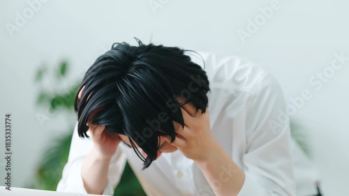 Young man stress frustration anxiety holding head tense expression indoor bright office desk stressed young man holding his head hands with tense expression conveying frustration and anxiety