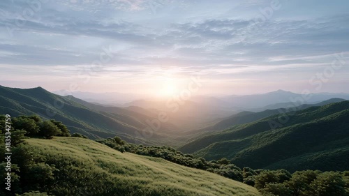 Breathtaking mountain landscape sunrise with rolling green hills, misty valley and soft morning sunlight casting peaceful atmospheric mood over layered ridges and forested slopes evoking calm