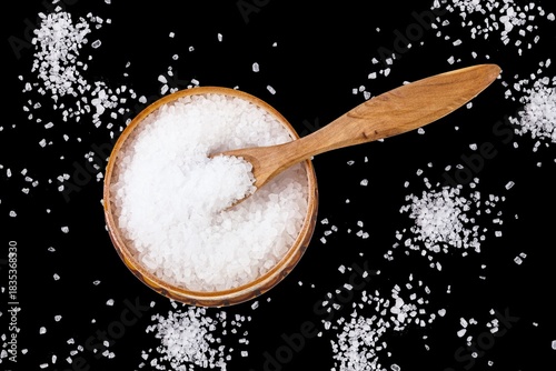 A bowl of coarse salt with a wooden spoon, surrounded by scattered salt grains, highlighting the essential role of salt in cooking and seasoning