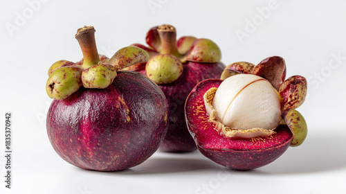 A close up shot of three mangosteens, one cut open, on a white surface showing the white flesh inside