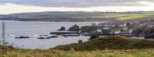 Panoramic view of St Abbs in Scotland with cliffs, harbor, and sea under cloudy light.