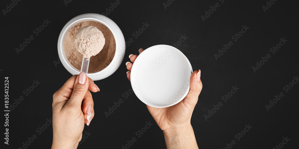 Naklejka premium Top view of female hand holding measuring scoop with chocolate whey protein powder above plastic jar on dark background with copy space, concept of sports nutrition and dietary supplements