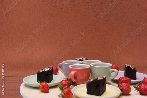 Wide dessert scene with pastel espresso cups, brownies, and strawberries arranged on plates against a textured terracotta background. Horizontal layout ideal for menus, cafés, and lifestyle visuals.