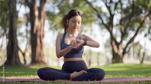 Asian adult woman checking fitness tracker practicing yoga meditation for health and wellness in a peaceful outdoor park