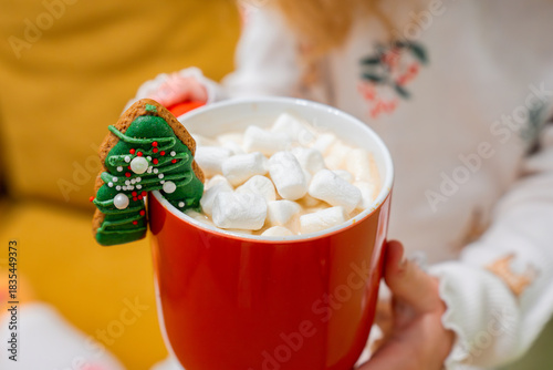 Little child holds a mug of cocoa and marshmallows on the couch