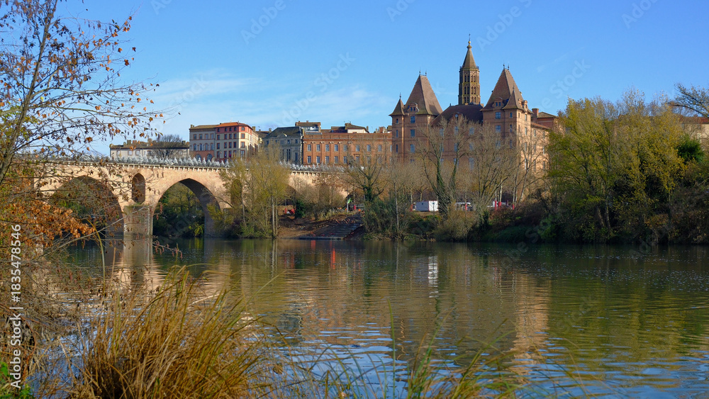 Obraz premium Charming Montauban with historical architecture and ancient stone bridge over tranquil river under clear blue sky during beautiful autumn day