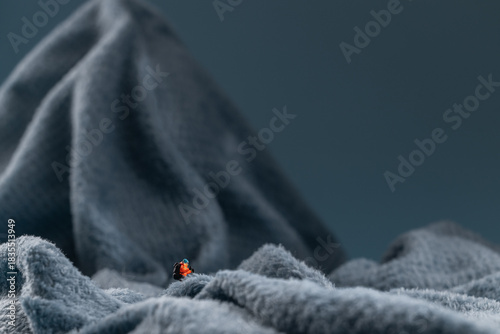 A miniature mountain climber figurine on a fuzzy fleece lining resembling a snow-covered surface, with a blurred background of a mountain or ice wall