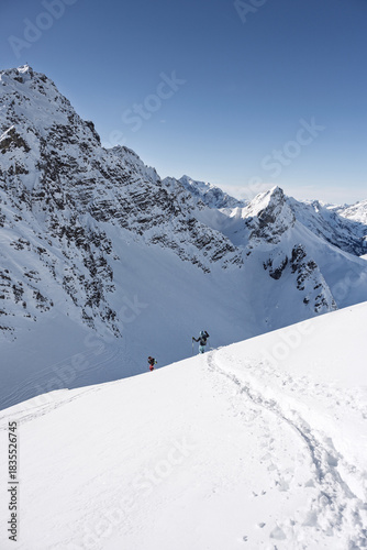 Two ski tourers descending toward the ski depot in a snowy alpine landscape during a winter backcountry adventure.