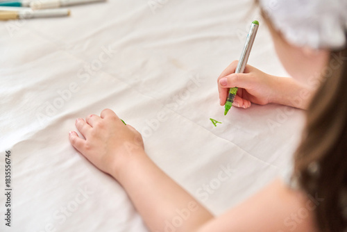 Child writing letter on white fabric with green marker